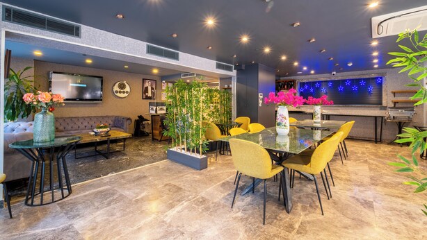 Un moderno vestíbulo de hotel con zona de comedor, televisor de pantalla plana y plantas decorativas.