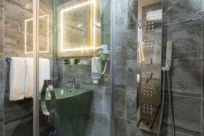 Un baño moderno con ducha acristalada, lavamanos verde y un espejo grande con marco iluminado.