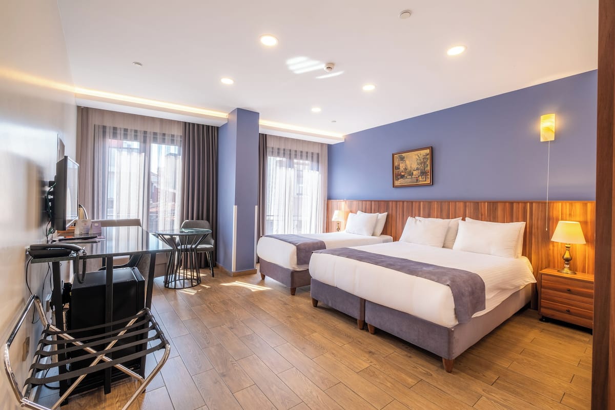 A hotel room with two beds, a desk, a chair, a TV, and a lamp.