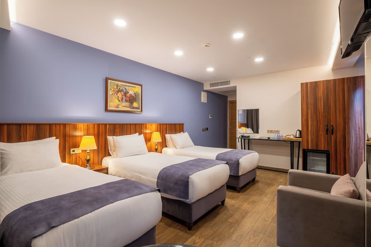 A hotel room with two beds, a desk, a chair, and a small kitchenette.