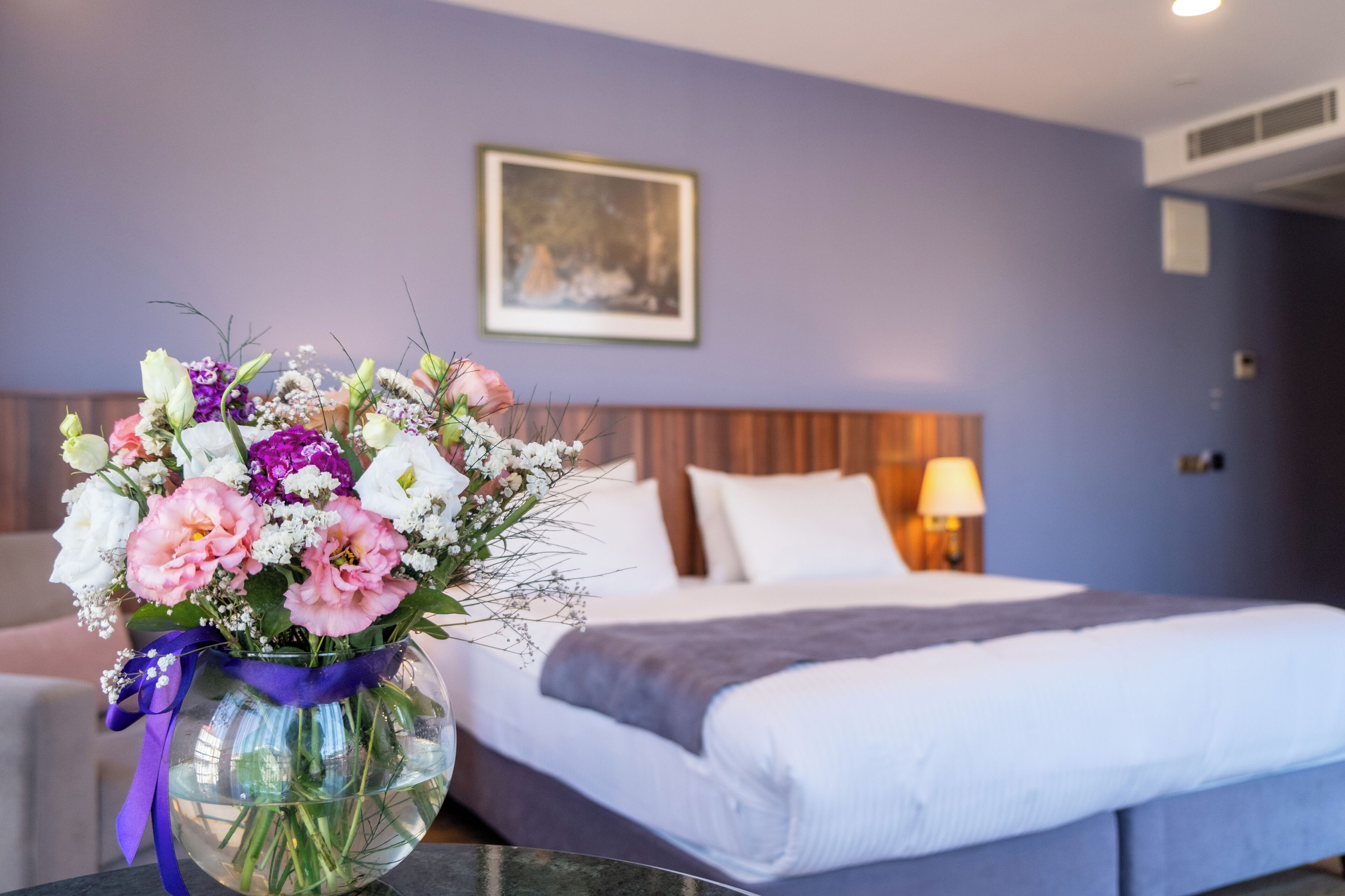 A hotel room with a bed, a nightstand, a lamp, and a vase of flowers on the table.