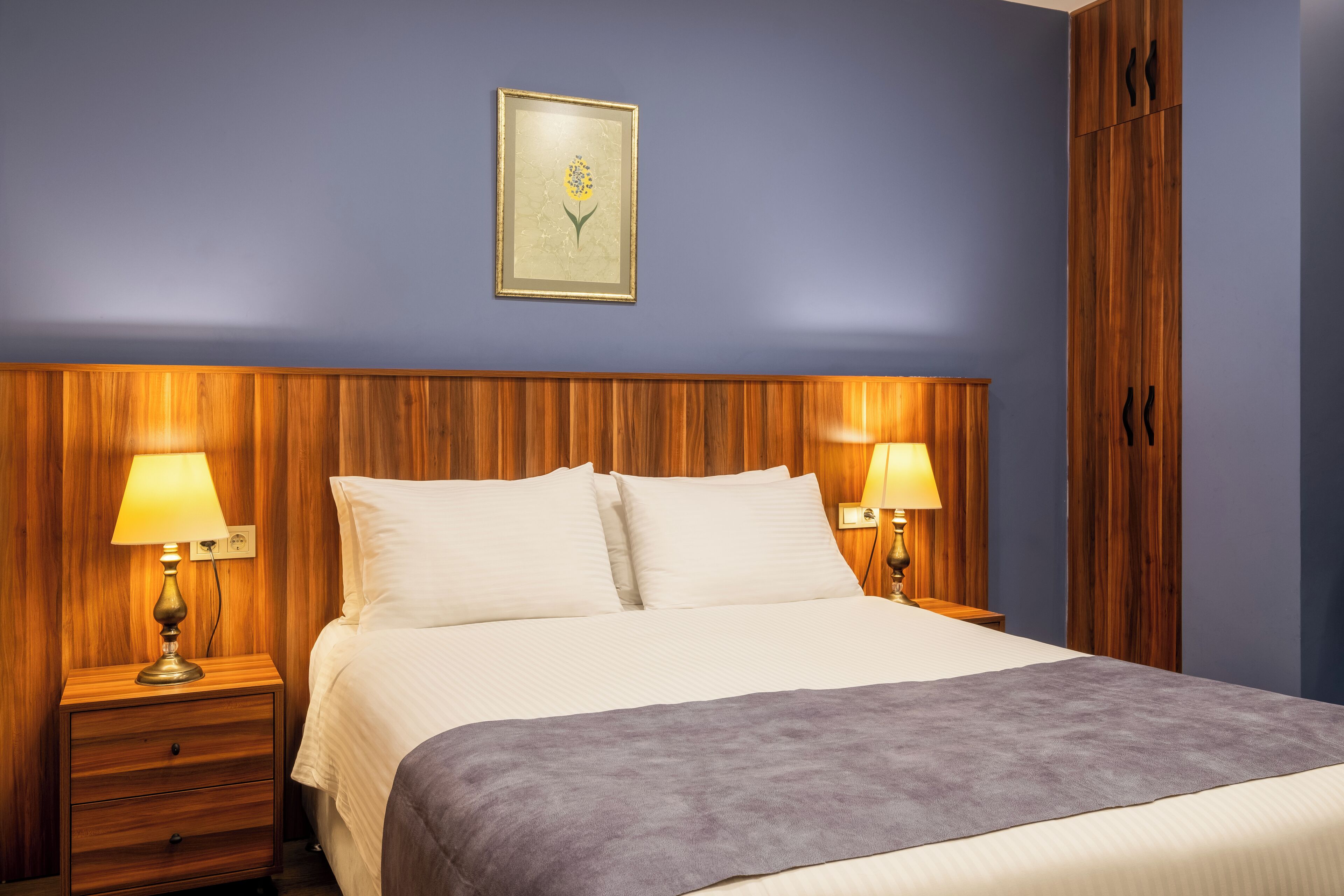 A neatly made bed with a wooden headboard, two bedside lamps, and a framed picture on the wall.