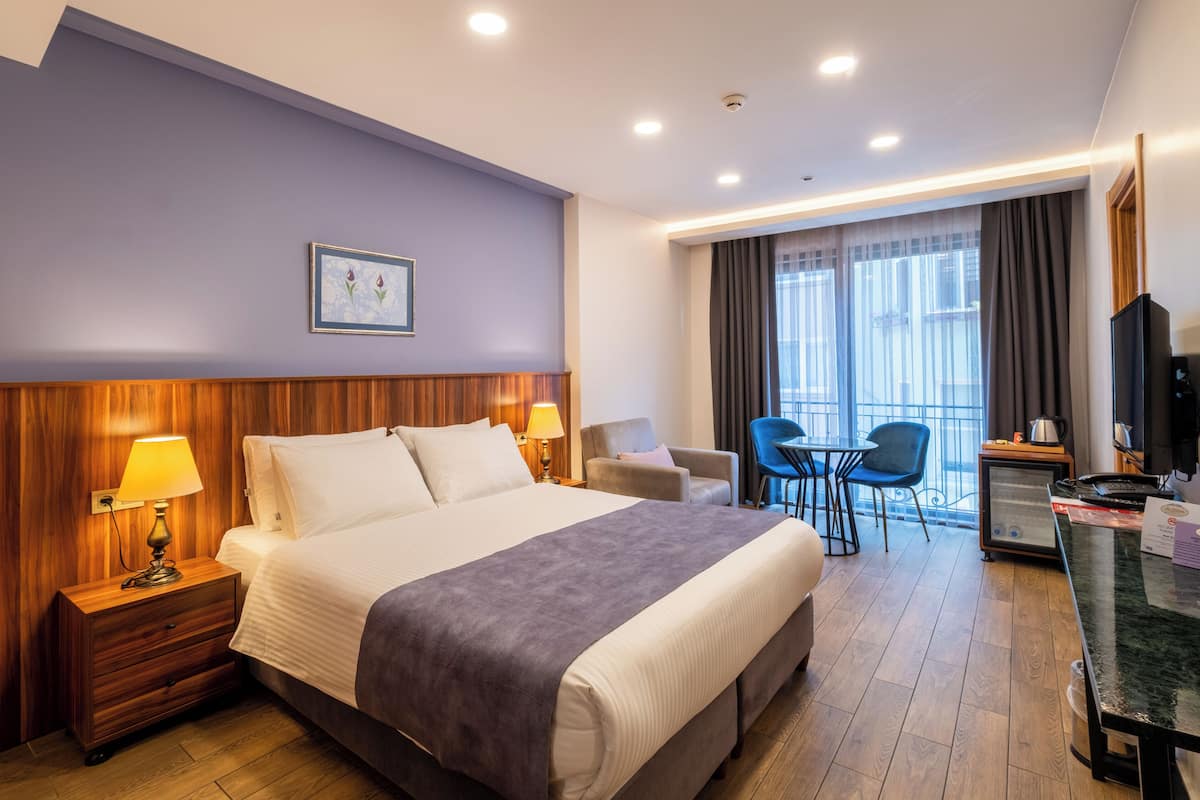 A hotel room with a large bed, bedside lamps, a desk with a computer, a chair, and a view of the outdoors through the window.