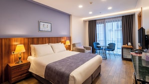 Habitación de hotel con una cama grande, lámparas de noche, un escritorio con una computadora, una silla y vista al exterior por la ventana.