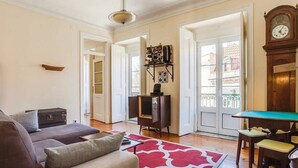 A living room with a sofa, a red patterned rug, a billiards table, and a clock on the wall. - JOIVY Lovely 3BR Apt w/ workspace, nearby Botanical Garden of Lisbon (Lisboa)