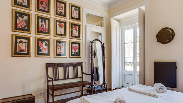 A hotel room with a bed, a wooden bench, a mirror, and a wall with framed pictures. - JOIVY Lovely 3BR Apt w/ workspace, nearby Botanical Garden of Lisbon (Lisboa)
