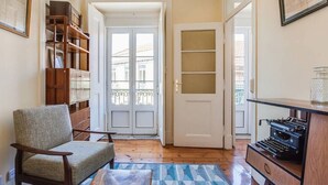 A hallway with a wooden floor, a chair, a bookshelf, a door with glass panels, and a desk with a typewriter. - JOIVY Lovely 3BR Apt w/ workspace, nearby Botanical Garden of Lisbon (Lisboa)