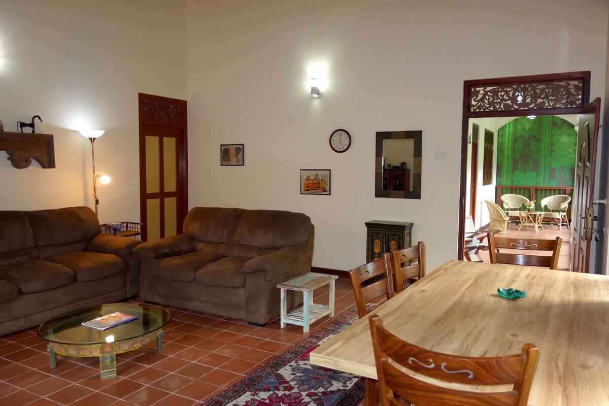 A living room with two sofas, a coffee table, a dining table with chairs, a small side table, and a decorative mirror.