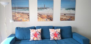 A blue sofa with two decorative pillows featuring seashells and a starfish, set against a wall with three framed beach scenes.