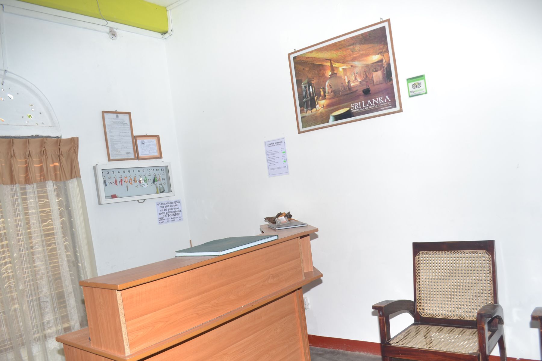 Un mostrador de recepción, un certificado enmarcado, un calendario, un cartel y una silla tradicional en una habitación con paredes blancas.