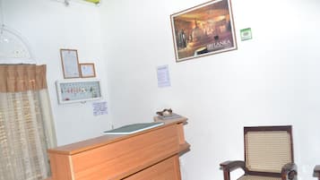 Un mostrador de recepción, un certificado enmarcado, un calendario, un cartel y una silla tradicional en una habitación con paredes blancas.