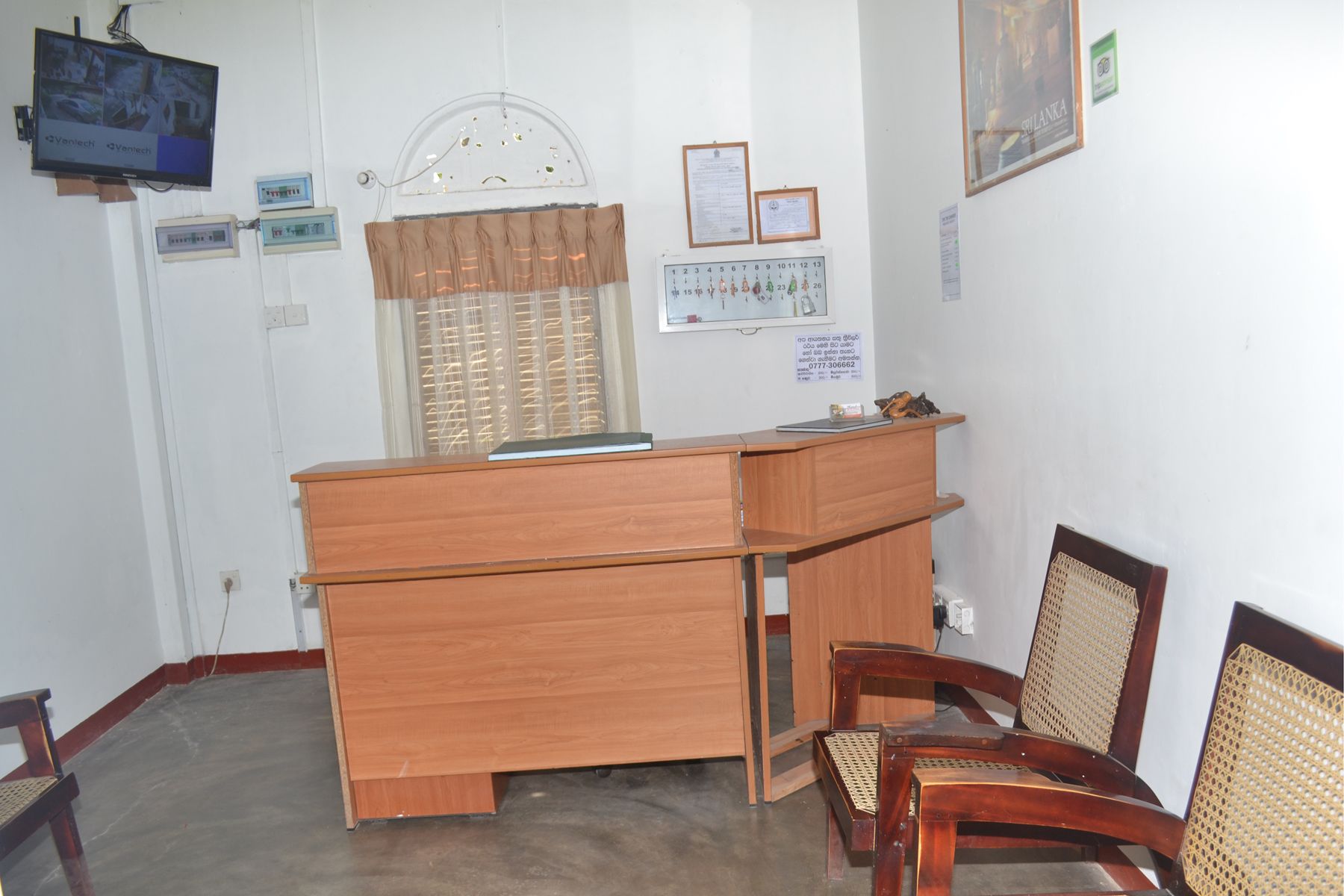 Une salle d’attente avec un bureau en bois, deux chaises, un téléviseur et une fenêtre équipée de stores.