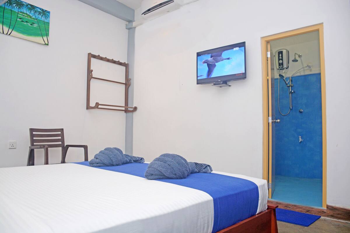 A bedroom with a bed, a TV, a shower, and a chair.