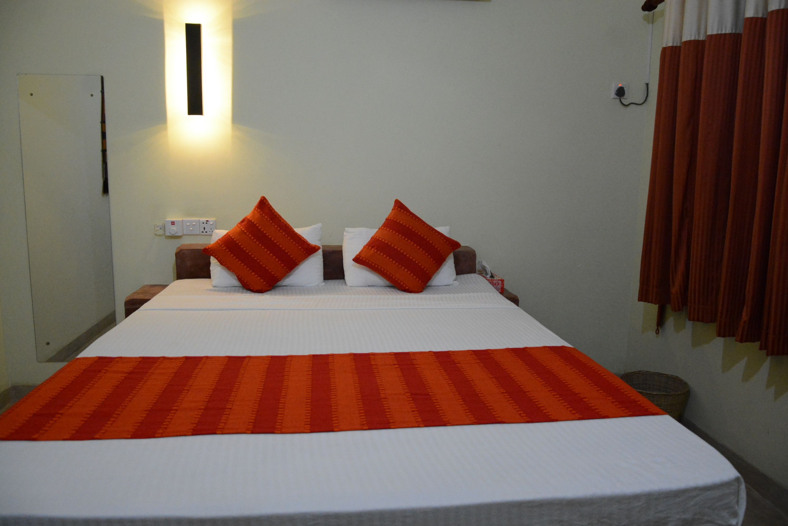 A hotel room with a bed, pillows, a bedside table, a lamp, and a curtain.