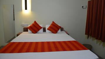 A hotel room with a bed, pillows, a bedside table, a lamp, and a curtain.