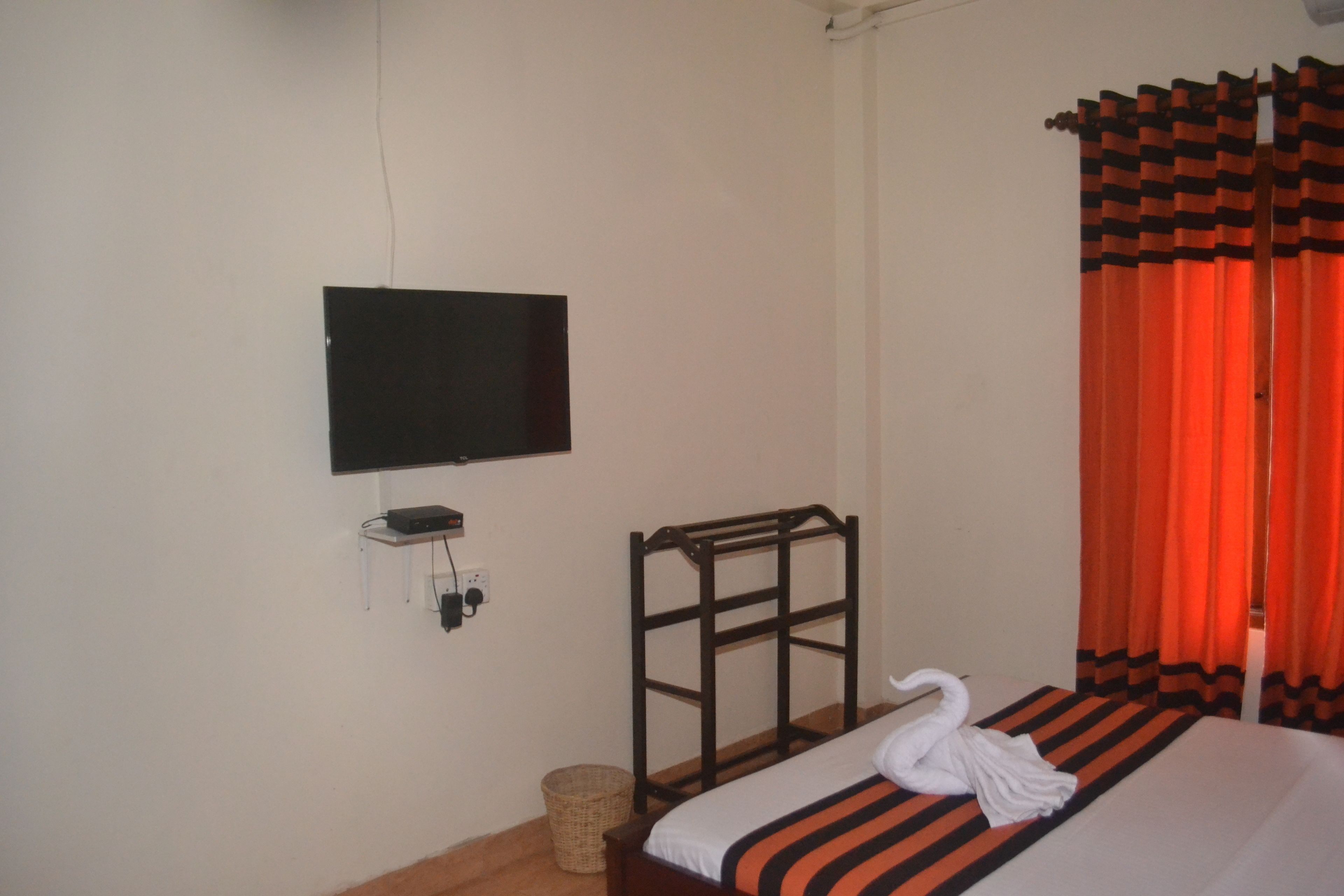 Une chambre d’hôtel avec un lit, un téléviseur fixé au mur, une tête de lit en bois et des rideaux orange.