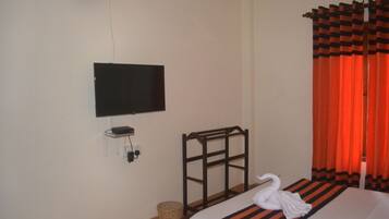 Une chambre d’hôtel avec un lit, un téléviseur fixé au mur, une tête de lit en bois et des rideaux orange.