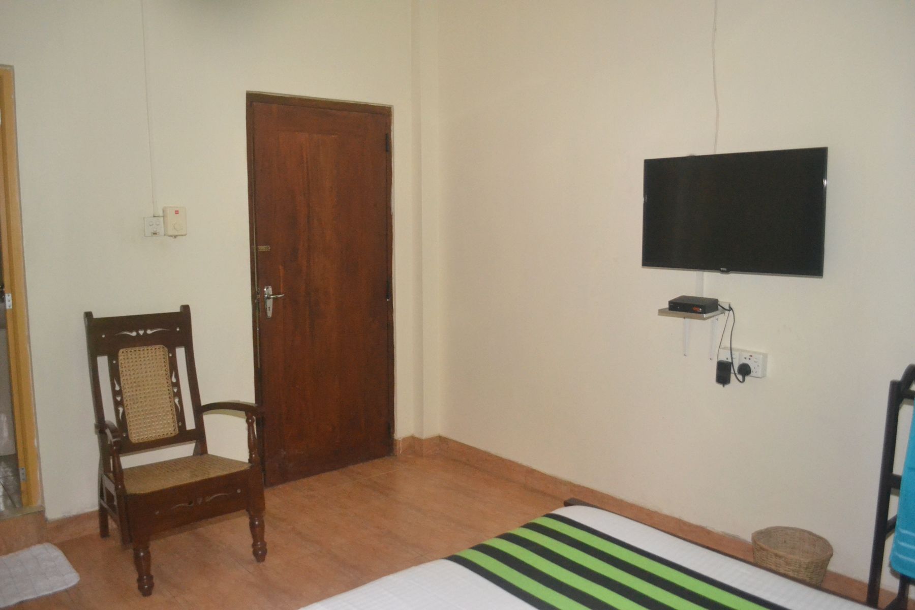 Un dormitorio con puerta de madera, una cama con colcha a rayas, un televisor montado en la pared y una silla.