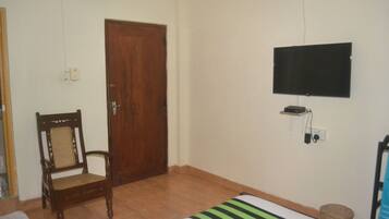 Un dormitorio con puerta de madera, una cama con colcha a rayas, un televisor montado en la pared y una silla.
