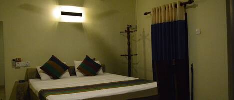 A hotel room with a bed, a ceiling fan, an air conditioner, a nightstand, and a window with curtains.