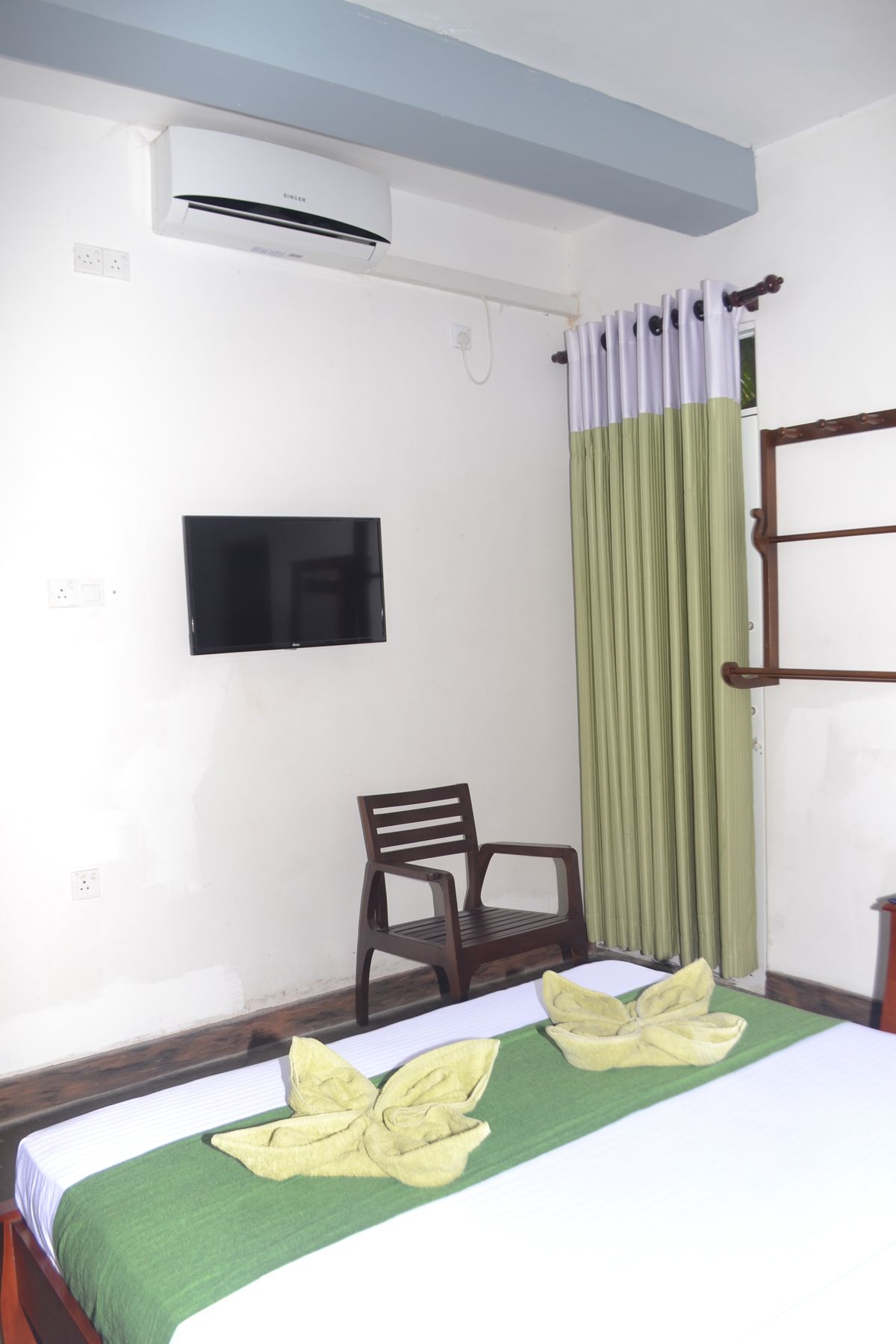 A hotel room with a bed, a chair, an air conditioner, a TV, and a window with curtains.