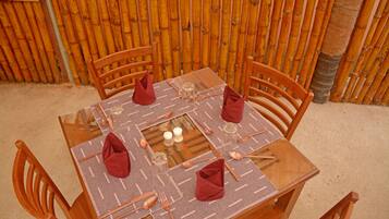 Una mesa cuadrada con cubierta de vidrio, rodeada por cuatro sillas de madera. La mesa está dispuesta con cubiertos, vasos y servilletas.