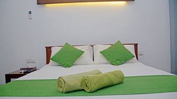 Una cama bien hecha con toallas y almohadas verdes, una mesita de noche con control remoto y una lámpara fijada a la pared.
