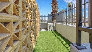 A narrow outdoor area with artificial green turf, a palm tree, and a metal fence. - Desert Moon Motel (Las Vegas)