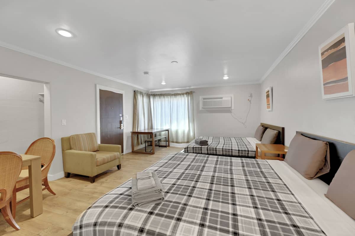 A hotel room with two beds, a sofa, a dining table, and chairs.