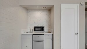 A compact kitchen with white cabinetry, a built-in microwave, and a stainless steel refrigerator. - Desert Moon Motel (Las Vegas)