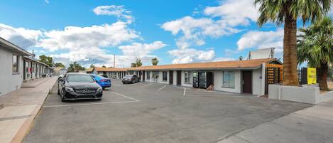 A parking lot with several cars, a building with a flat roof, and a palm tree.