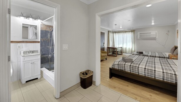 A bedroom with a bed, a small table, and a chair. There is a bathroom with a sink, mirror, and shower. - Desert Moon Motel (Las Vegas)