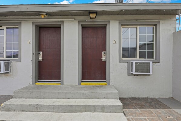 A building with two doors, numbered 18 and 17, and two air conditioning units on the exterior wall.
