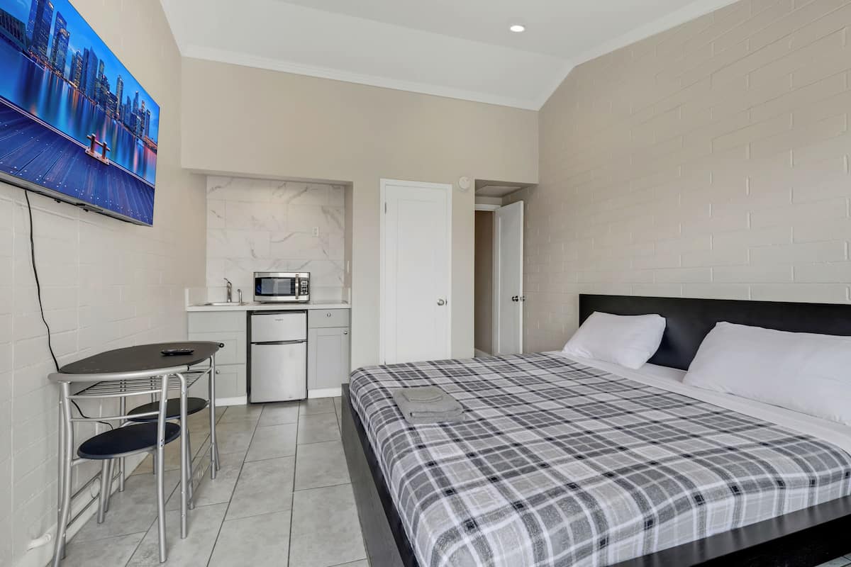 A modern hotel room with a bed, a desk with a chair, a microwave, and a painting on the wall.