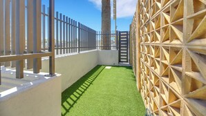A narrow pathway with artificial green grass, a metal fence, and a wooden lattice wall. - Desert Moon Motel (Las Vegas)