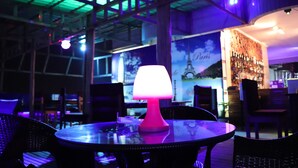 Una mesa con una lámpara rosa en un ambiente interior tenuemente iluminado, con techo verde y un cartel del Torre Eiffel.