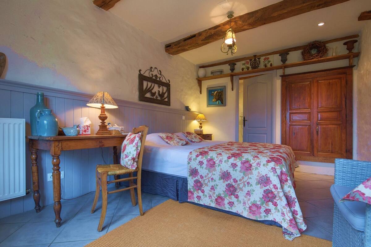 Ein Schlafzimmer mit einem Bett, einem Holzstuhl, einem Tisch mit Lampe und einer Kommode.