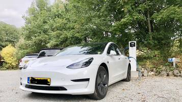 A white electric car parked at a charging station with trees in the background.