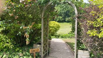 A wooden archway leading to a gravel path, surrounded by lush greenery and a sign reading 'Gite.'
