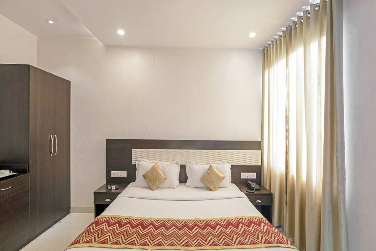 A hotel room with a bed, nightstands, a wardrobe, and a window with curtains.