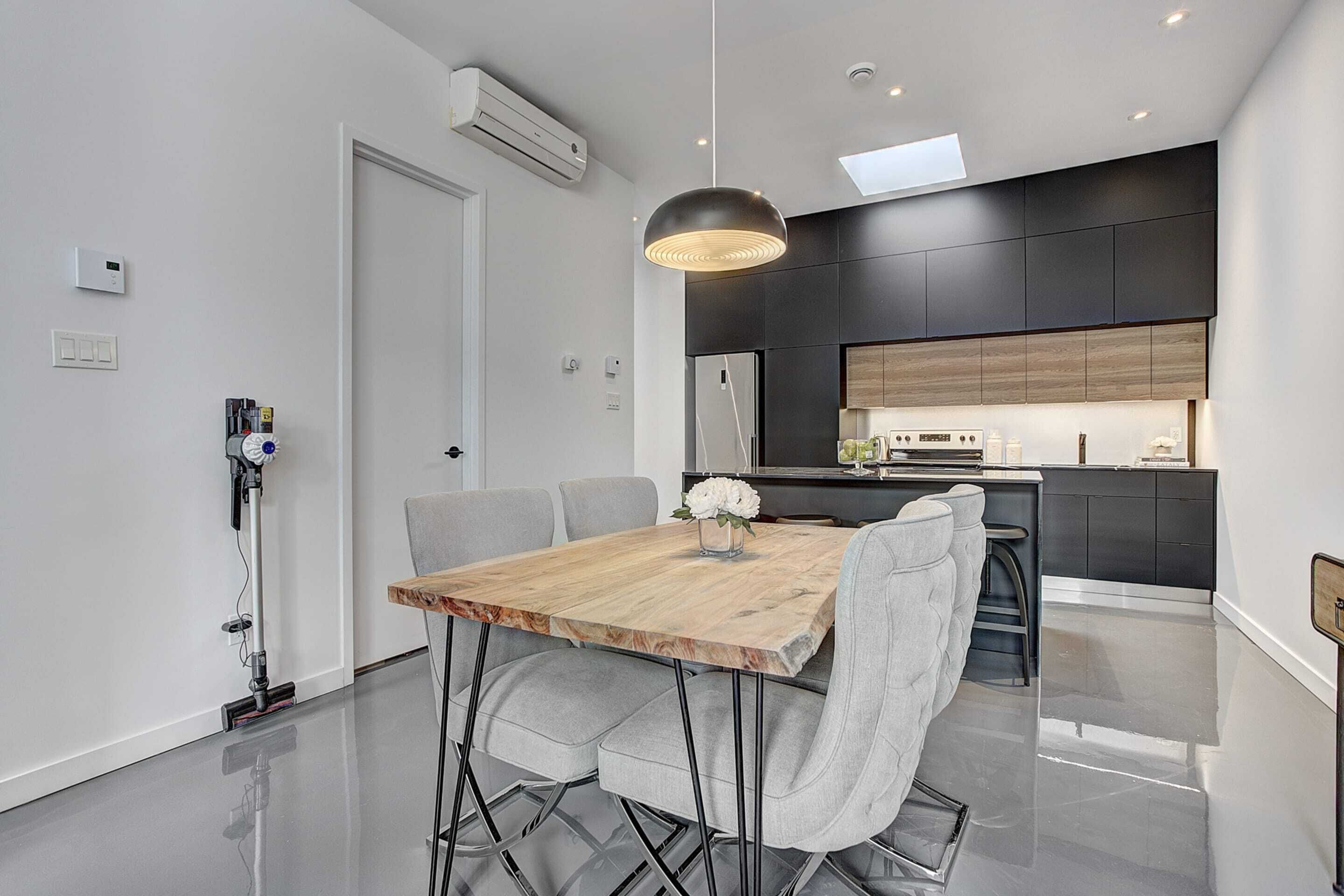 A modern kitchen with dark cabinetry, a wooden dining table, and a pendant light.