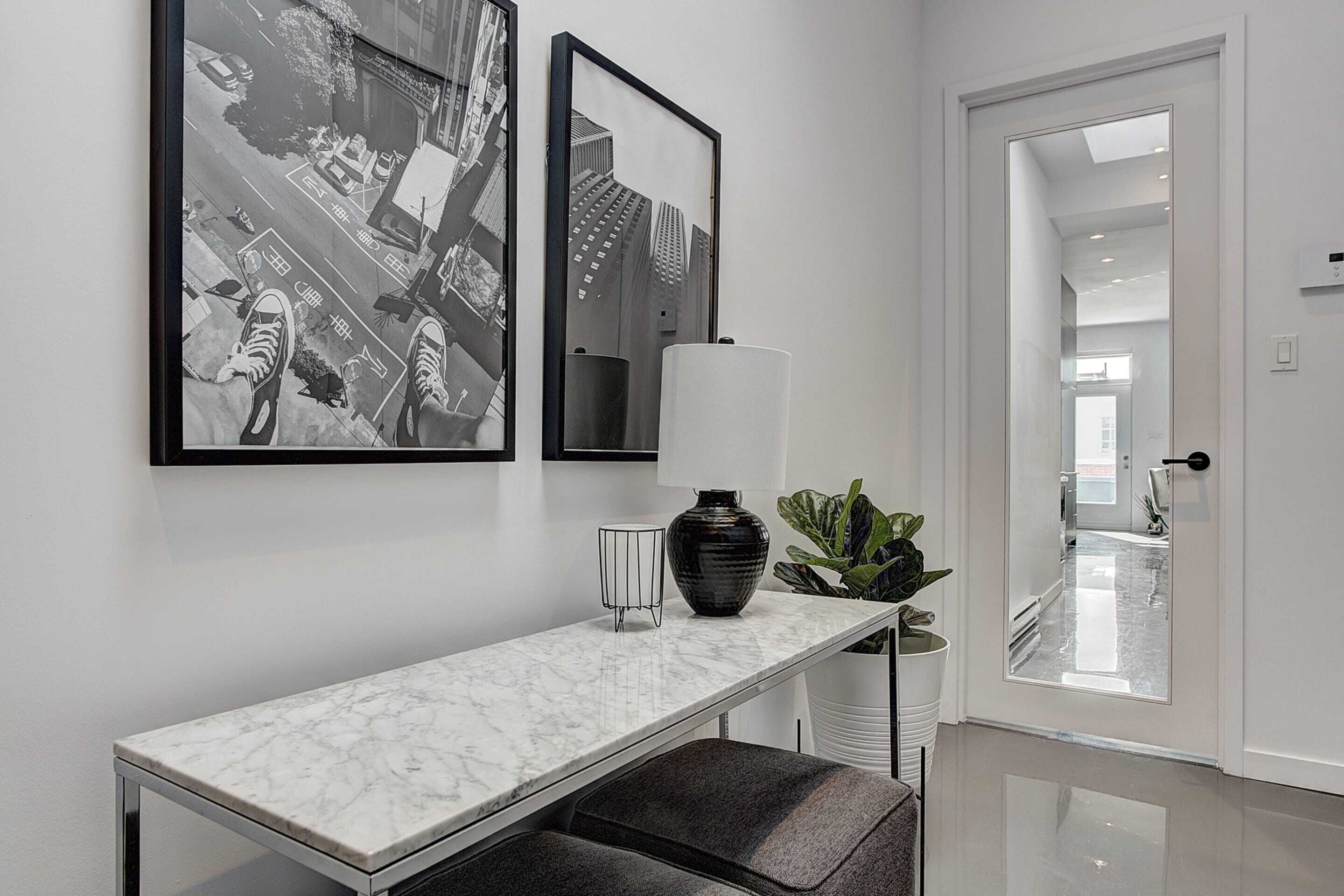 En modern hall med ett konsolbord i marmor, två svartvita fotografier, en vas och en krukväxt.