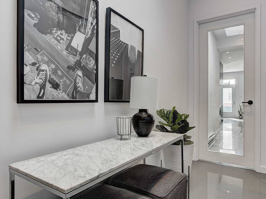 En modern hall med ett konsolbord i marmor, två svartvita fotografier, en vas och en krukväxt.