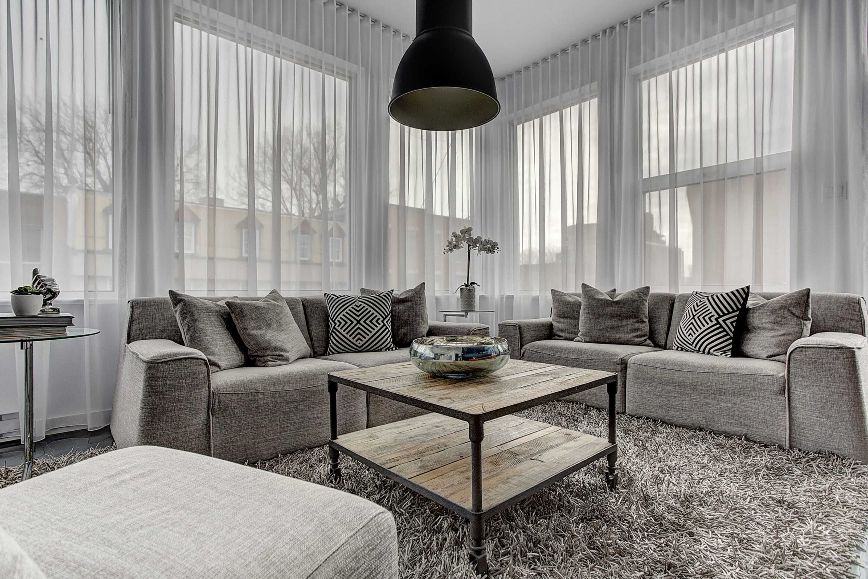 A modern living room with a sectional sofa, a coffee table, and sheer curtains.