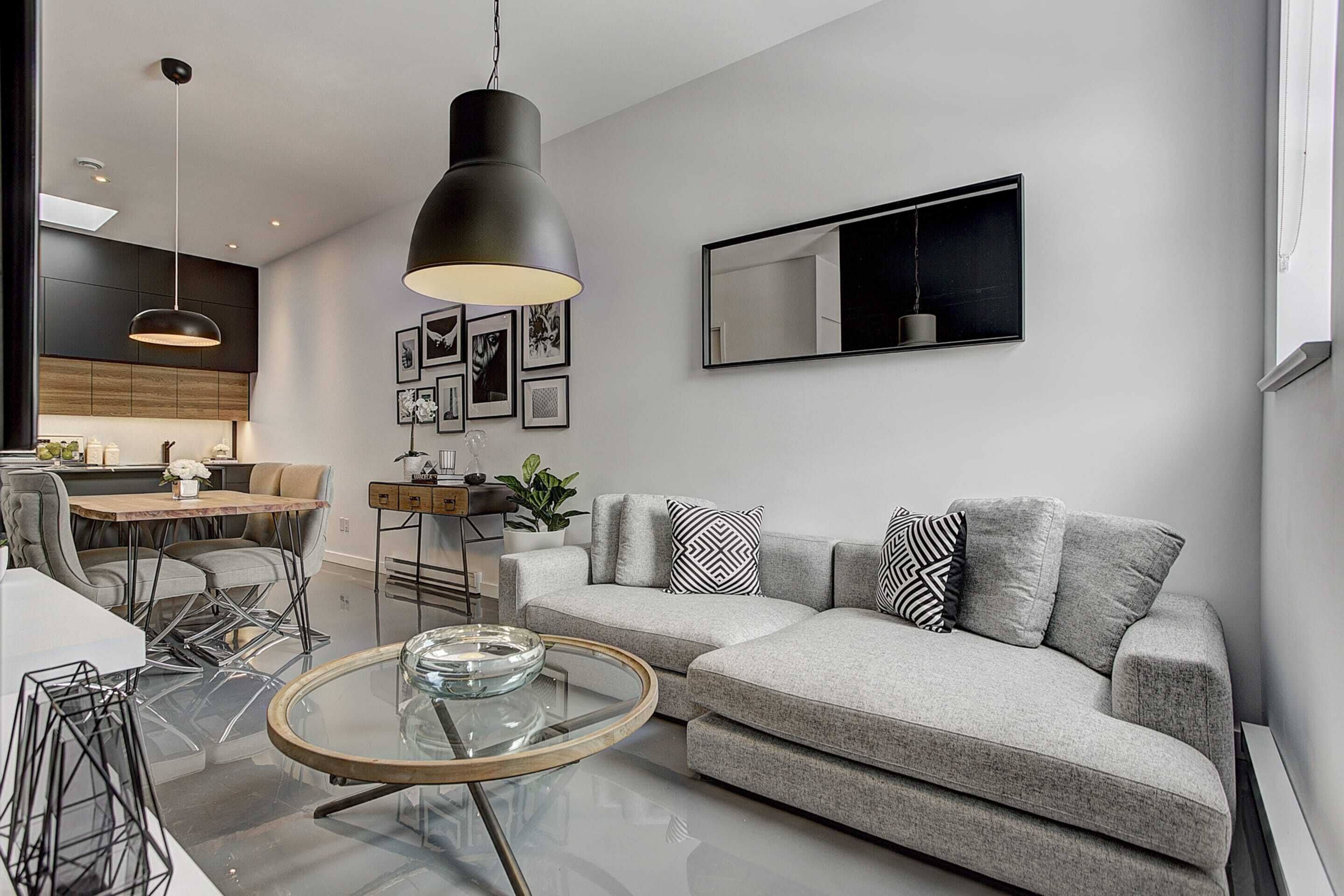 A modern living room with a grey sofa, a glass coffee table, and a dining area with a wooden table and chairs.