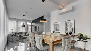 A modern living room with a dining area, featuring a wooden dining table, grey upholstered chairs, and a large pendant light. - Les Lofts du Centre (Montreal)