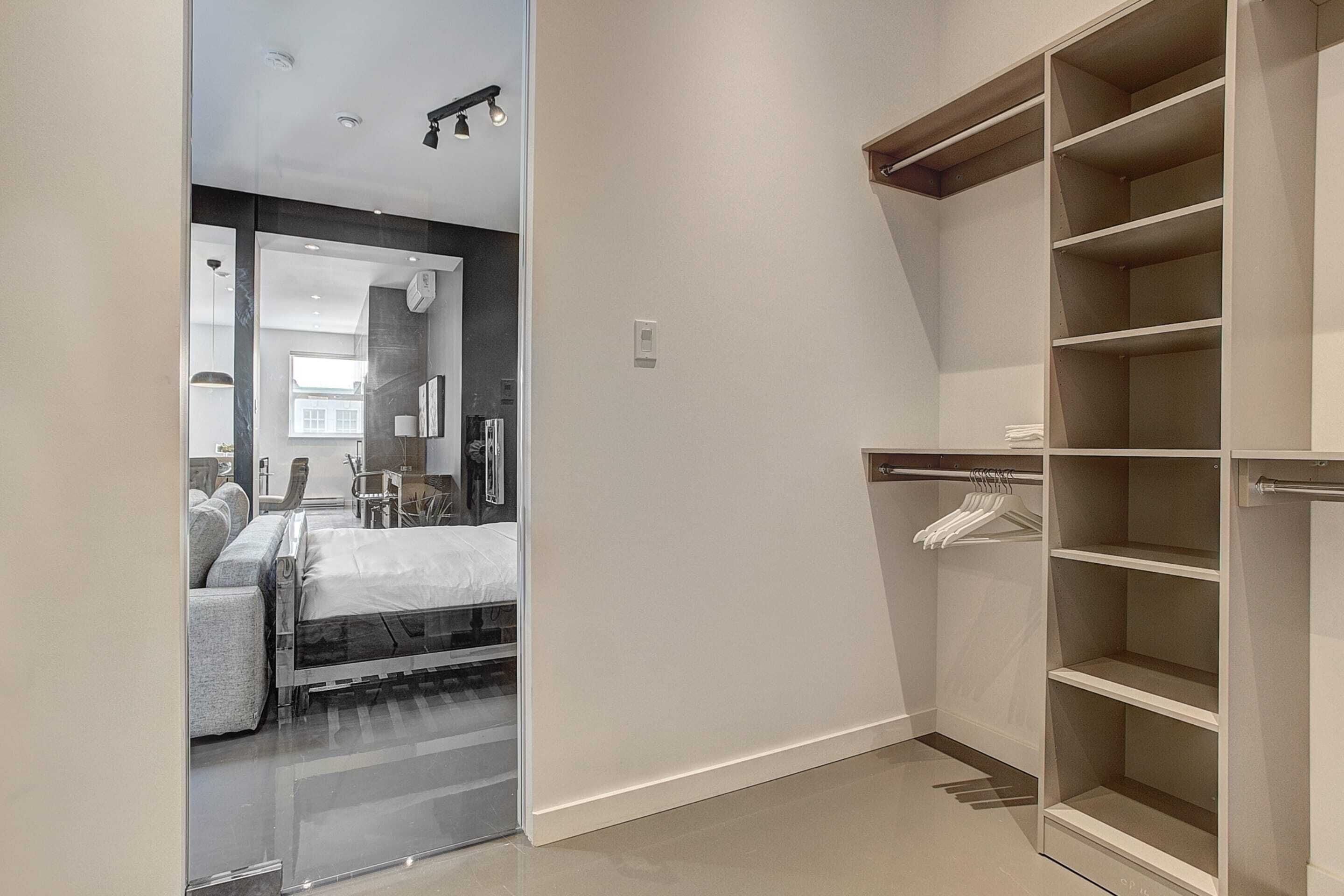 A modern bedroom with a bed, bedside table, and a walk-in closet with shelves.