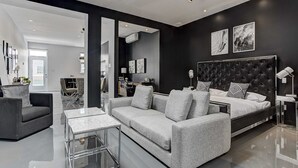 A modern living room with a grey sofa, a glass coffee table, and a large bed with a black headboard. - Les Lofts du Centre (Montreal)