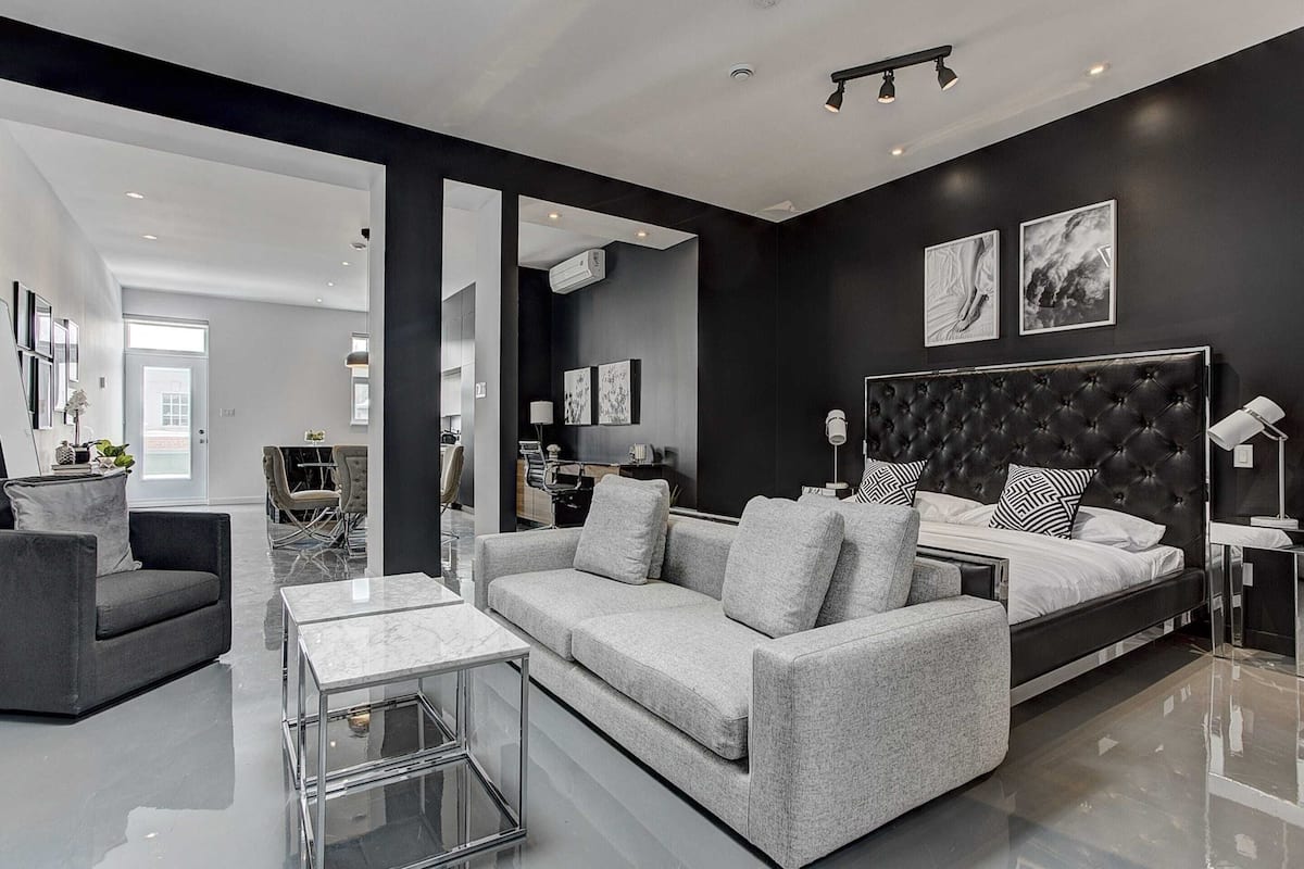 A modern living room with a grey sofa, a glass coffee table, and a large bed with a black headboard.