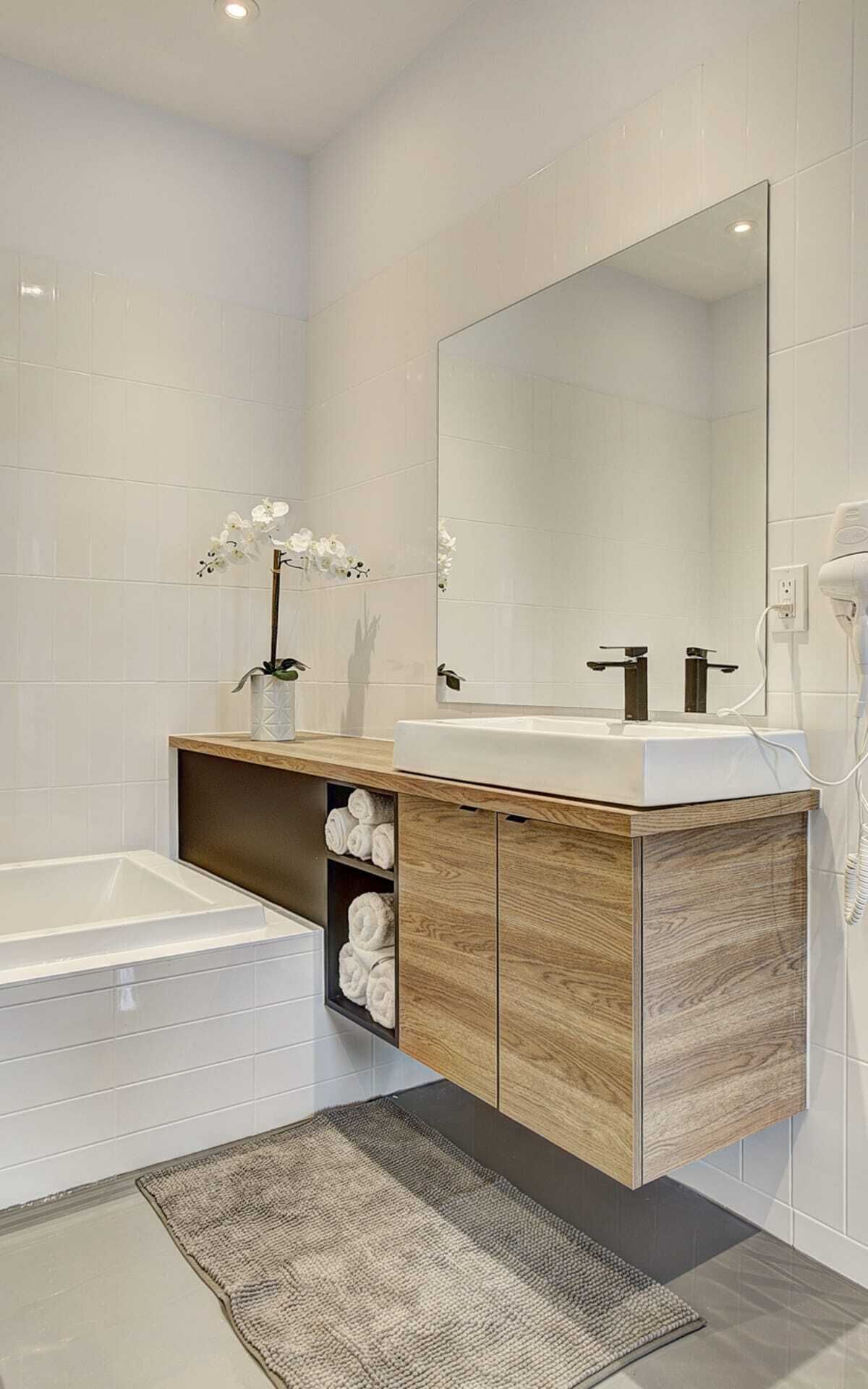 Ein modernes Badezimmer mit einem Holzwaschtisch, einem großen Spiegel, einer Badewanne und einer kleinen Ablage mit Handtüchern.